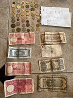Photo showing a variety of old foreign coins arranged in rows with nine paper currency bills below, handwritten note 'Lot #43 Old foreign currency Paper + Coin poor condition'. Coins used as weights for paper bills excluded from count.