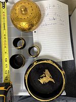 Overhead view of large gold-color bowl with lid, three small black cups, and large black bowl with gold motif.
