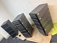 Three dark plastic drawer units arranged in descending size order, two tall with wheels, one smaller without visible wheels