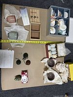 Overview of miscellaneous household items on a board, showing ceramic cups, small wooden box, wrapped bowls, small dark bowls, and figurines