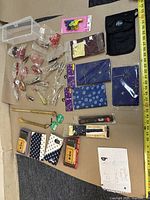 Photo showing all items arranged on beige and dark surface, including chopsticks, writing brushes with boxes, cloth cases with traditional patterns, small accessories, and wrapped figurines.