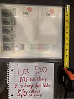 Photo of the plastic folder containing various stamps including visible Nippon 20 stamps in a block on the first page, with a measuring tape for size reference.