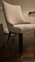 Side view of a beige velvet modern dining chair with curved back and dark wooden legs on hardwood floor under indoor lighting.