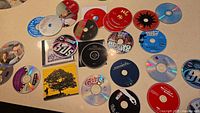 20 music CDs spread out on a countertop, showing disc labels and some album covers like Grease and a yellow tree cover.