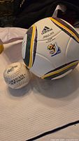 Adidas Jabulani FIFA World Cup size 5 soccer ball and official Gale Force softball on a white fabric background.