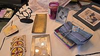 Photo showing an assortment of home decor items including napkin holders, brass serving dish, coasters, picture frames, a candle jar, and folded napkins.