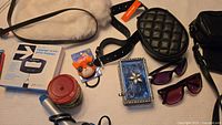 Photo showing the assortment of items including the white and black faux leather bag, black leather belt, black quilted oval bag, jewelry box, luggage scale, sunglasses, curling iron, hot water bottle with white fur cover, Fossil wallet, and a red container.