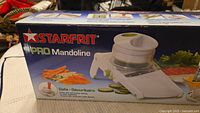 Box front showing Starfrit PRO Mandoline branding and illustration of the mandoline slicer with sliced vegetables.