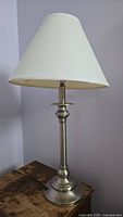 Front view of traditional brushed nickel table lamp with white fabric cone shade on wooden surface.