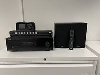 Front view of Yamaha receiver with black digital audio component dock on top, alongside two Polk speakers and a remote control.