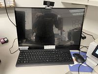 Dell all-in-one desktop computer setup with integrated monitor, black keyboard, optical mouse, and attached webcam on top of the monitor.