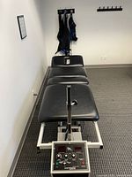 Full view of the black padded spinal decompression table with mechanical controls near the base, placed against a wall in a clinical room.