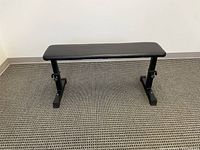 Photo of a flat adjustable exercise bench with a black padded seat and sturdy black metal frame