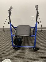 Blue medical walker viewed from front showing seat, hand brakes, and caster wheels.