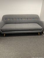 Front view of gray fabric sofa showing multicolor buttons on the backrest and wooden legs