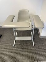 Front view of the phlebotomy chair showing contoured seat, backrest, and dual padded arm supports on a metal base with footrest.