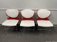 Three white and red chairs with curved backrests and metal legs on grey carpet, showing a different style than the leather sofa and chairs.