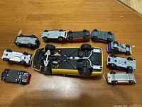 Top-down view of underside of 10 toy cars arranged with the larger yellow toy car at the bottom and nine smaller cars in a semi-circle above it showing undercarriage details and wheels.