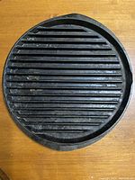 Top-down image of a round cast iron griddle showing ridged grilling surface on wooden table.