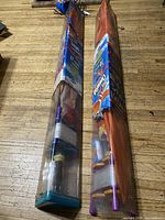 Two packaged kites laid flat on wood floor, visible packaging with kite sticks and accessories inside.