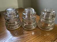 Three clear glass insulators displayed on wooden surface showing shape and size.