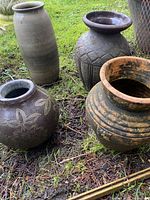 Four ceramic/terracotta pots grouped outside on grass and soil showing overall shapes and textures