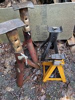 Four metal jack stands of different sizes and colors placed on ground outdoors with visible rust and wear.