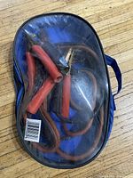 Jumper cables inside a blue oval carrying case with clear plastic top, showing orange cables with red and black insulated clamps.