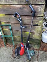 Full view of the Black & Decker edger and Toro weed trimmer standing outdoors against wooden siding