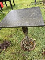 Full view of the side table showing square marble top and decorative brass base on grass.