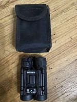 Top view of black soft carrying case and folded Bushnell binoculars on wooden surface