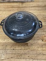 Cast iron Dutch oven with clear glass lid shown from an angle on a wooden surface.