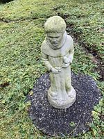 Full front view of concrete statue of St. Francis on a circular asphalt base in grass