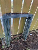 Stack of galvanized metal lawn sign holders leaning against fence, showing multiple units stacked together.