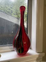 Front view of the red glass vase showing the slender neck and bulbous base with light reflecting on the glass surface.