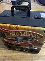 Front side of black wheeled Hot Wheels car carrier case showing logo and graphic.