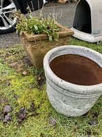 Photo of two outdoor planters on grass; one square older planter with plants inside, one round white ceramic planter in front, both outdoors showing weathering and aging.