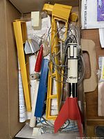 Box with plastic Estes rocket body featuring red fins, wires, metal launch rod, and various plastic components laid out.