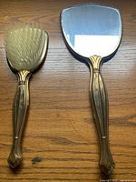Top view of the vintage handheld mirror and hair brush showing front side with mirror and brush bristles on wooden surface.