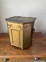 Front and side view of brass coal scuttle sitting on wooden surface showing rivet and pattern details.