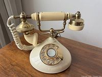 Side view of vintage rotary dial cradle phone showing cream body and brass details.