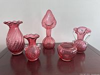 Full set of five cranberry glass vases arranged on table showing size and shape variations