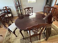 Full view of oval dining table with leaf leaning against side and four chairs around.