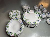 Overall view of the dishes showing stacked dinner plates, bowls, salad plates, and several cups arranged on a floor.