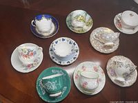 Overview of nine English porcelain cups and saucers with varied floral and decorative designs arranged on a dark wooden surface.
