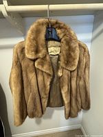 Front view of the Giddings brown fur coat with large collar hanging on a hanger.