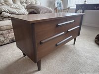 Side angle view of blanket box showing rectangular shape, tapered legs, and horizontal wooden handles.