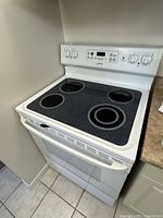 Front angled view of the white Moffat electric stove showing four glass-ceramic burners, oven door, and control panel with knobs and digital display.