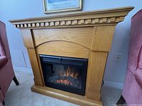 Front view of oak wooden electric fireplace showing the mantel design and flame effect inside.