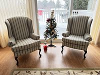 Pair of wing back chairs with striped upholstery near sliding glass doors and a small Christmas tree between them.
